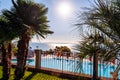 Sunny outdoor pool behind the fence with crystal water, parasols and deck chairs with Garda lake and Sirmione city on the