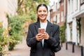 Sunny portrait of a newly entrepreneur young woman in her 25s, black suit, holding a phone smiling, looking in camera Royalty Free Stock Photo