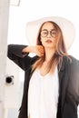 Sunny portrait pretty sexy stylish young woman in trendy glasses in fashionable black jacket in white t-shirt in straw hat Royalty Free Stock Photo