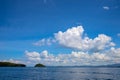 Sunny sea and sky landscape with distant island. Idyllic tropical cloudscape with green island