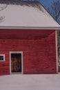 Brown barn door against the bright red clapboards against a snowy white field on a bright winters day. Royalty Free Stock Photo