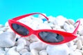 Sunny stylish glasses in bright red rim white sea stones, blue background, concept
