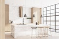Sunny stylish kitchen with marble tabletop, city view from squared transparent wall and wooden decoration wall parts.