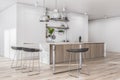 Sunny stylish spacious kitchen room with wooden furniture, black bar chairs and kitchen utensils and dishes on light wall