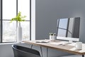 Sunny stylish workspace with city view from big window, plane in white vase and modern monitor on wooden table