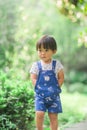 A lively little boy in blue overalls stands among the bushes in the park