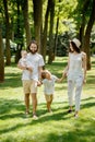 Sunny summer day. Happy young family dressed in the white casual clothes walks in the park. Royalty Free Stock Photo