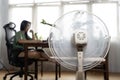 Sunny summer in front of the working fan, suffering from the summer heat. Unhappy Asian woman sitting in front of fan at work Royalty Free Stock Photo