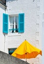 Sunny view of a white house with blue window and an orange sunshade f