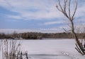 Sunny winter landscape with a frozen lake and clear water around a house with a pier against a row of trees under an Royalty Free Stock Photo