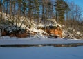 Winter landscape with red sandstone cliffs on the bank of the river Salaca, the sun shines on the trees and the river bank, the Royalty Free Stock Photo