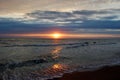 Sunrise on the beach with water waves and a cloudy, purple sky in the background Royalty Free Stock Photo