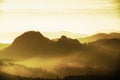 Sunrise in a beautiful mountain of Czech-Saxony Switzerland. Sharp hills increased from foggy background, the fog is orange due to Royalty Free Stock Photo