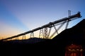 Sunrise behind silhouetted stockpile and conveyor belt in a copper mine at the Atacama Desert