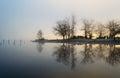 Sunrise through the fog creating reflections of the trees on a lake.