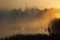 Sunrise on a foggy lake. The morning city in a haze in the background. Mirror surface of water Royalty Free Stock Photo