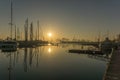 Sunrise in the harbor of Valencia, the sun rises between docked sailboats and cargo port cranes