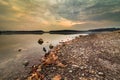 Sunrise with heavy clouds at Blue Marsh with the lake and fallen leaves on its rocky edge in the foreground