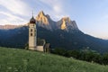 Sunrise landscapes of Church St. Valentin on grassy hilltop with view of rugged peaks of Mountain Schlern with alpenglow in backgr