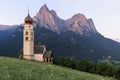 Sunrise landscapes of Church St. Valentin on grassy hilltop with view of rugged peaks of Mountain Schlern with alpenglow in backgr