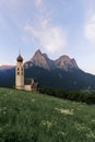 Sunrise landscapes of Church St. Valentin on grassy hilltop with view of rugged peaks of Mountain Schlern with alpenglow in backgr