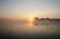 Sunrise over the foggy lake with the reflection of sun and trees in the water. Early fresh morning landscape. Mist on the water, Royalty Free Stock Photo