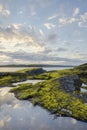 Sunrise over green rocky island. Clouds reflecting in water