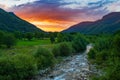 Sunrise over Idyllic valley in the Italian Alps. Stream flowing through blooming alpine meadow and lush green woodland amid Royalty Free Stock Photo