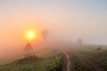 Sunrise over mountain field. Haystacks and road in misty autumn Royalty Free Stock Photo