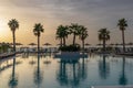 Sunrise over the pool and sunbeds. On the background of the sea coast. Big palm trees Royalty Free Stock Photo