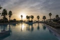 Sunrise over the pool and sunbeds. On the background of the sea coast. Big palm trees Royalty Free Stock Photo