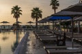 Sunrise over the pool and sunbeds. On the background of the sea coast. Big palm trees Royalty Free Stock Photo