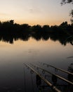 Sunrise reflections over peaceful English lake with three fishing rods on buzzers Royalty Free Stock Photo