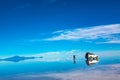 Sunrise on Salar de Uyuni in Bolivia covered with water, car and man in salt flat desert and sky reflections