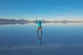 Sunrise on Salar de Uyuni in Bolivia covered with water, woman tourist on salt flat desert and sky reflections