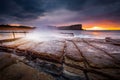 Sunrise sky and waves crash onto rocky beach shore