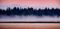 Sunrise Sunset on Lake with Mist Rising from Water Pine Trees and Mountains in Background Royalty Free Stock Photo