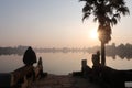 Sunrise , sunset over lake in angkor wat with sun reflecting in the water and palm and snake statue in foreground Royalty Free Stock Photo