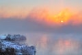 Sunrise time over the winter river. An orange fog spreads over the water and obscures the horizon. Reeds stand in the snow near Royalty Free Stock Photo