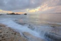 Sunrise under a stormy sky with clouds illuminated by the golden sunlight at the rocky beach