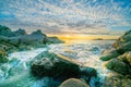 Sunrises over distant horizon along beach from rocky foreground