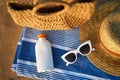 Sunscreen bottle on striped towel next to woven bag, straw hat, and white sunglasses on sandy beach suggests smart sun Royalty Free Stock Photo