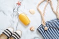 Sunscreen cream in a yellow bottle, striped sandals and beach bag, seashells on marble background. Beauty cosmetic product for ski Royalty Free Stock Photo