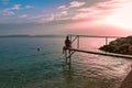 Sunset on the Adriatic Sea. A young woman sits on a mooring bridge and admires the scenery