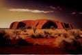 Sunset in the arid Australian desert with red dirt and large rock formation