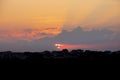 Sunset on the background of forest and village houses, dark color tone.The red sun hides behind the clouds, the rays break through Royalty Free Stock Photo