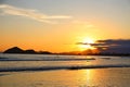 Sunset at the beach. In the background silhouettes of mountains, reddish sky. Beach with reflections in the sand.