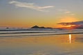 Sunset at the beach. In the background silhouettes of mountains, reddish sky. Beach with reflections in the sand.