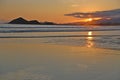 Sunset at the beach. In the background silhouettes of mountains, reddish sky. Beach with reflections in the sand.