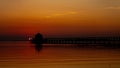 Sun setting over a long boardwalk pier by the sea